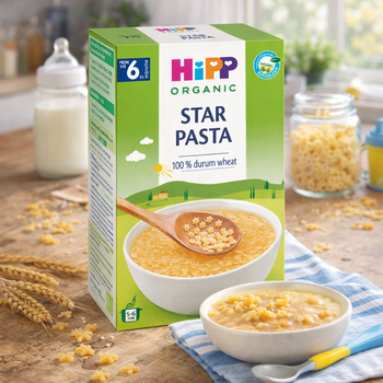 Hipp Organic Star Pasta packaging on a wooden table with pasta and a bowl.