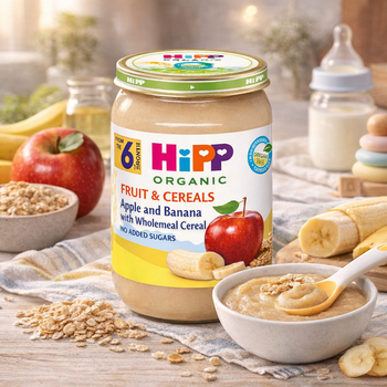 Hipp organic baby food jar with fruit and cereals on a table with apples, bananas, and a bowl of the product.