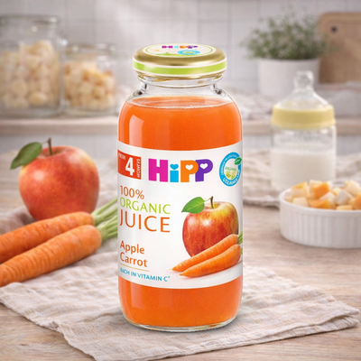 Bottle of HiPP 100% Organic Apple Carrot Juice on a wooden table with fruits and a blurred background.