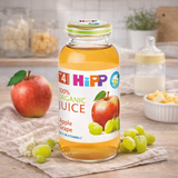 Bottle of HiPP 100% Organic Apple Grape Juice on a wooden table with fruits.