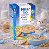 Hipp organic baby cereal packaging with a bowl of cereal, cookies, and a teddy bear on a wooden surface.