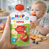 Hand holding a Hipp Organic Hippis baby food pouch with a child in the background