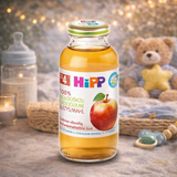 Hipp baby food bottle with apple illustration on a wooden surface with a teddy bear and baby items in the background.