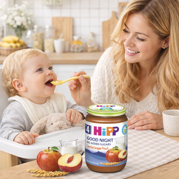 Woman feeding a baby with a spoon next to a Hipp Good Night jar in a kitchen setting