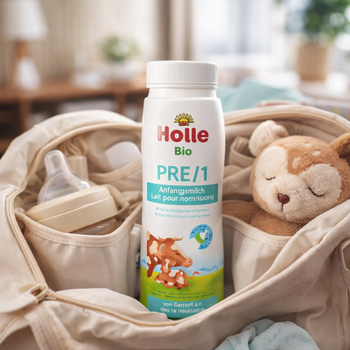 Holle Bio PRE/1 baby formula bottle in a crib with baby items