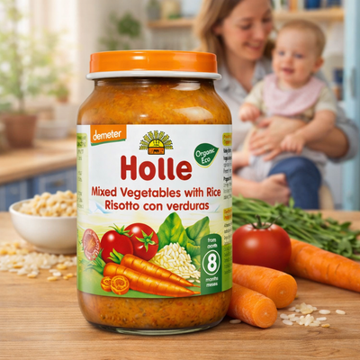 Holle organic baby food jar with vegetables and rice on a kitchen counter, featuring a woman and child in the background.