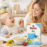 Woman feeding a baby with Holle Bio infant formula packaging in the foreground.