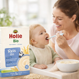 Woman feeding a baby with Holle Bio rice cereal packaging in the foreground.