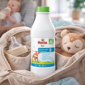 Holle organic baby formula bottle in a baby bag with a baby and teddy bear in the background