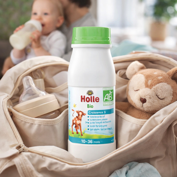 Holle organic baby formula bottle with a baby and teddy bear in the background