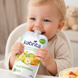 Child holding a kabrita fruit smoothie pouch with a bowl of fruit in the background