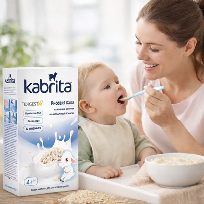 Woman feeding a baby with a bowl of cereal next to a box of Kabrita cereal.