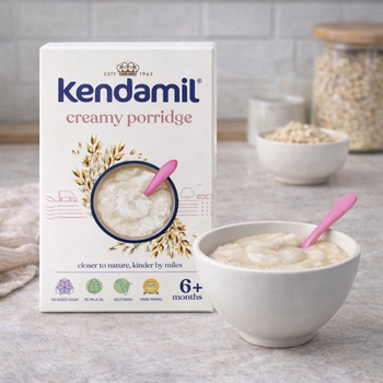 Kendamil creamy porridge packaging with a bowl of porridge and a spoon on a wooden surface.