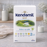 Kendamil goat follow-on milk packaging on a kitchen counter with milk bottles in the background.